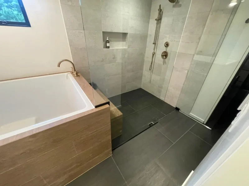 Modern walk-in shower with dark tile flooring and floating wood bathtub surround