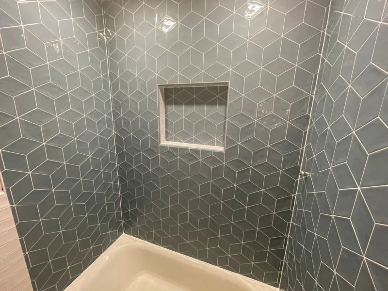 Blue-gray geometric cube-pattern shower tile with a recessed niche and white grout for a modern 3D effect