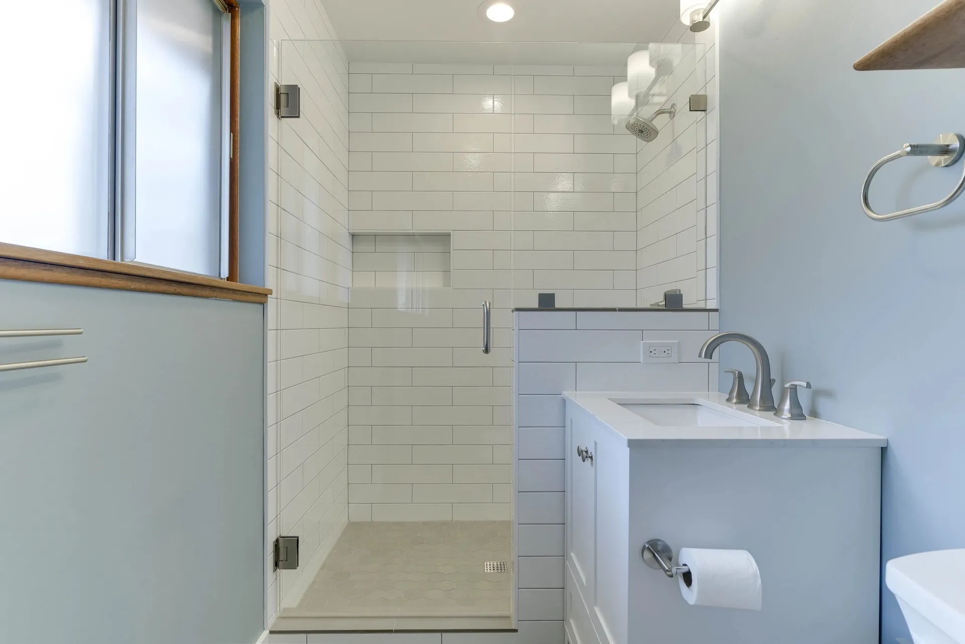 Compact white bathroom with subway tile shower, glass partition, and modern vanity sink