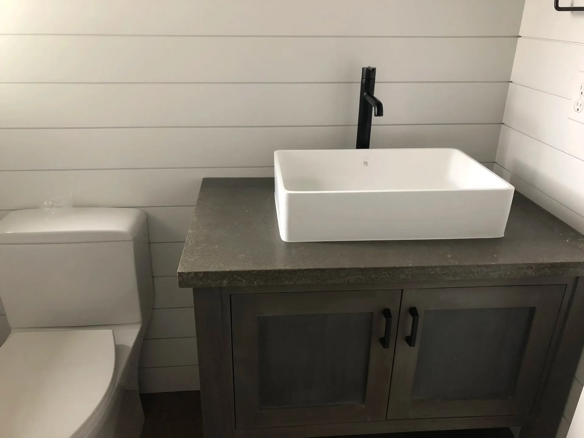 Modern bathroom vanity with vessel sink, matte black faucet, and white shiplap walls