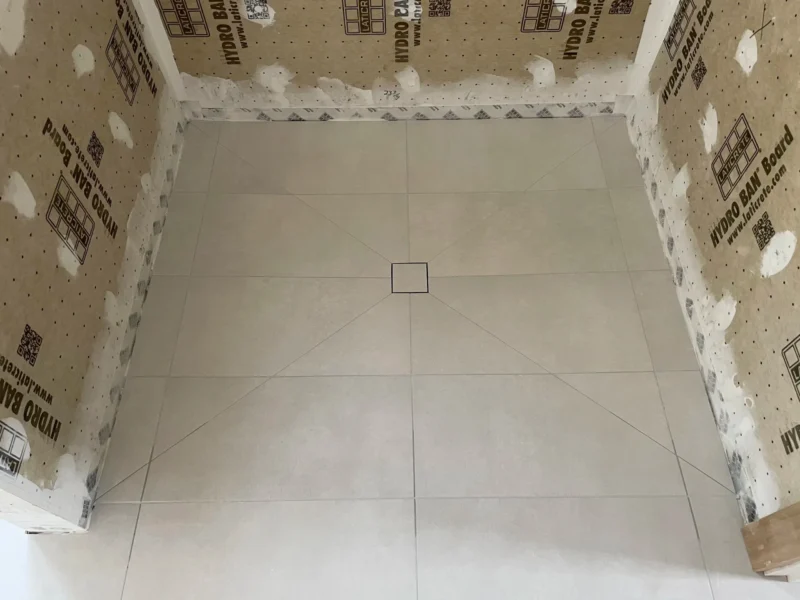 Large-format tiled shower base with centered square drain and waterproof backer board walls