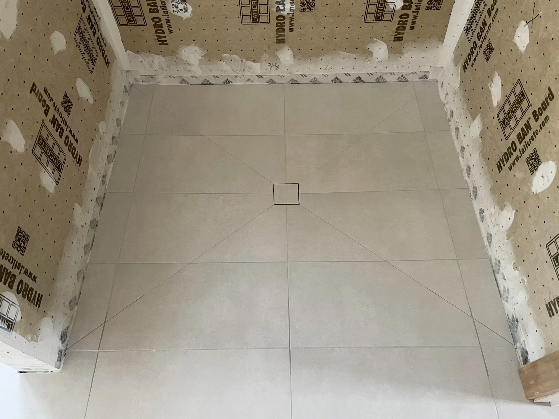 Large-format tiled shower base with centered square drain and waterproof backer board walls