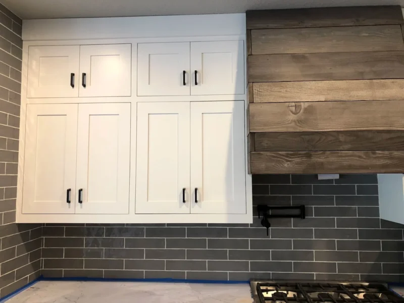 White shaker cabinets with gray subway tile backsplash and rustic wood vent hood accent