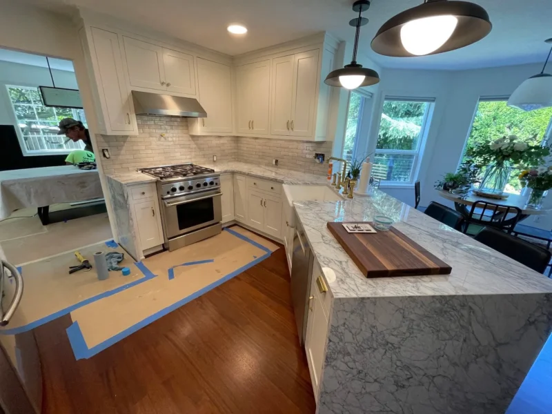 White kitchen with marble countertops, subway tile backsplash, and stainless gas range installation