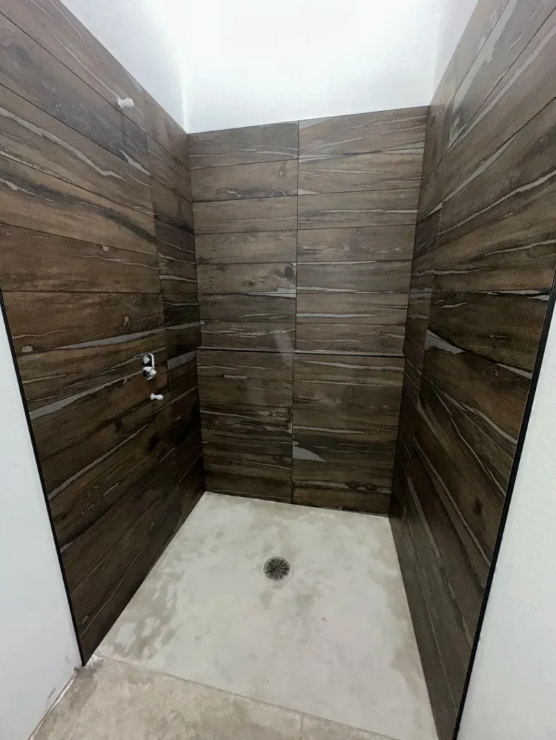 Dark wood-look tiled shower walls with minimalist concrete shower base and center drain