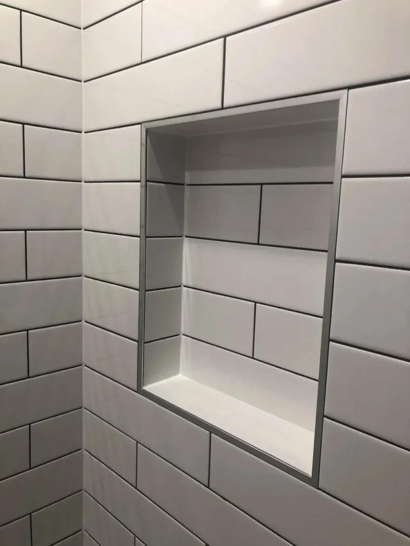 White subway tile shower niche with metallic trim and contrasting dark grout