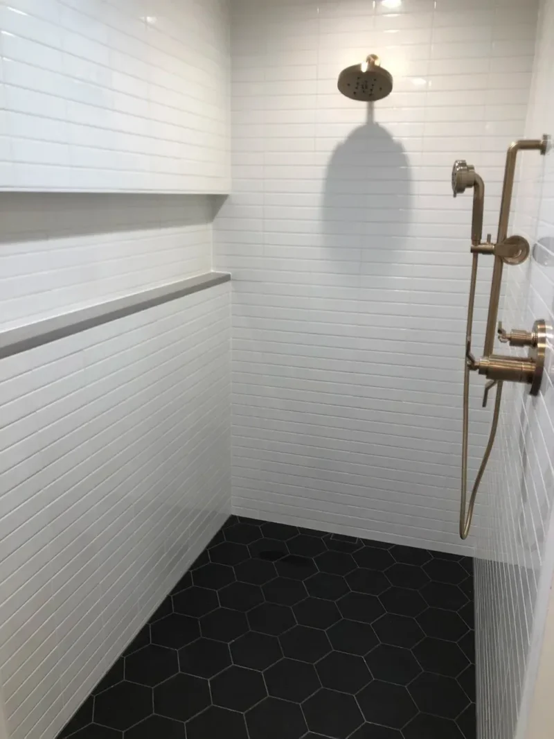 White tiled shower with black hexagon floor and brass fixtures