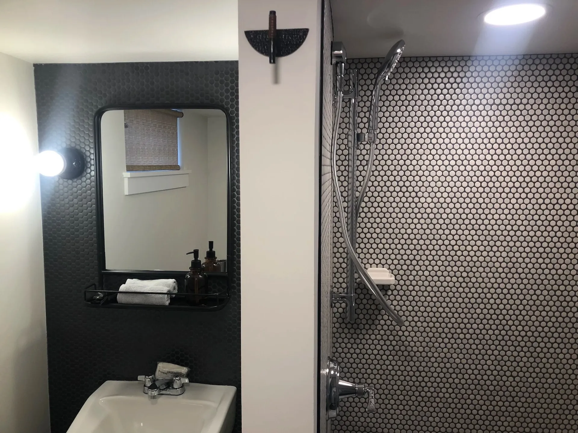 Compact bathroom with black penny tile walls and modern shower fixtures