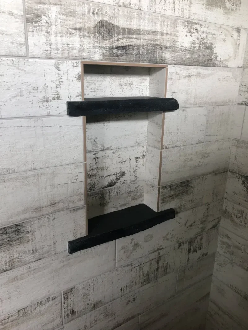 Recessed shower niche with black shelves and distressed wood-look wall tile