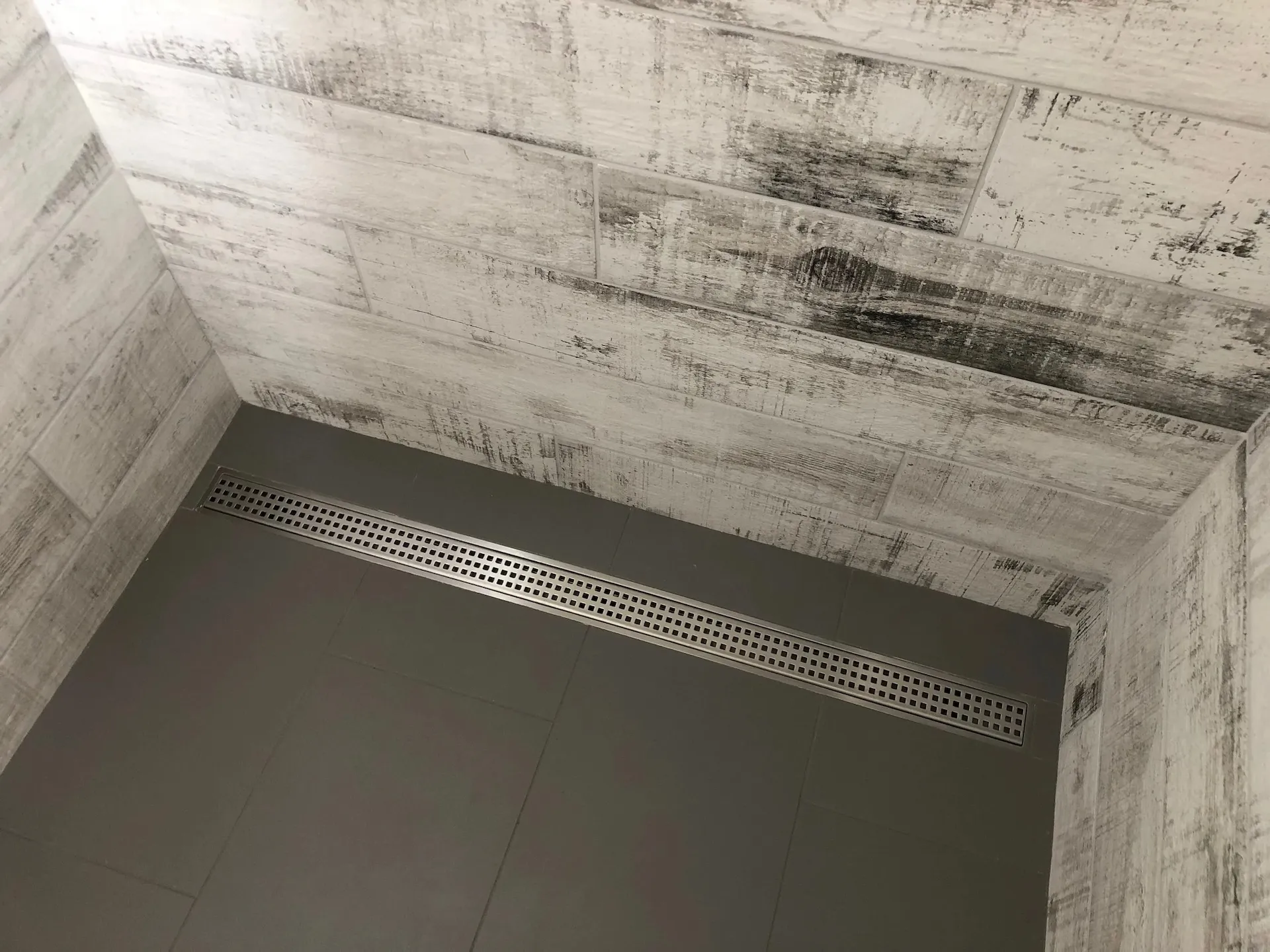 Linear shower drain with dark floor tile and rustic wood-look wall tile