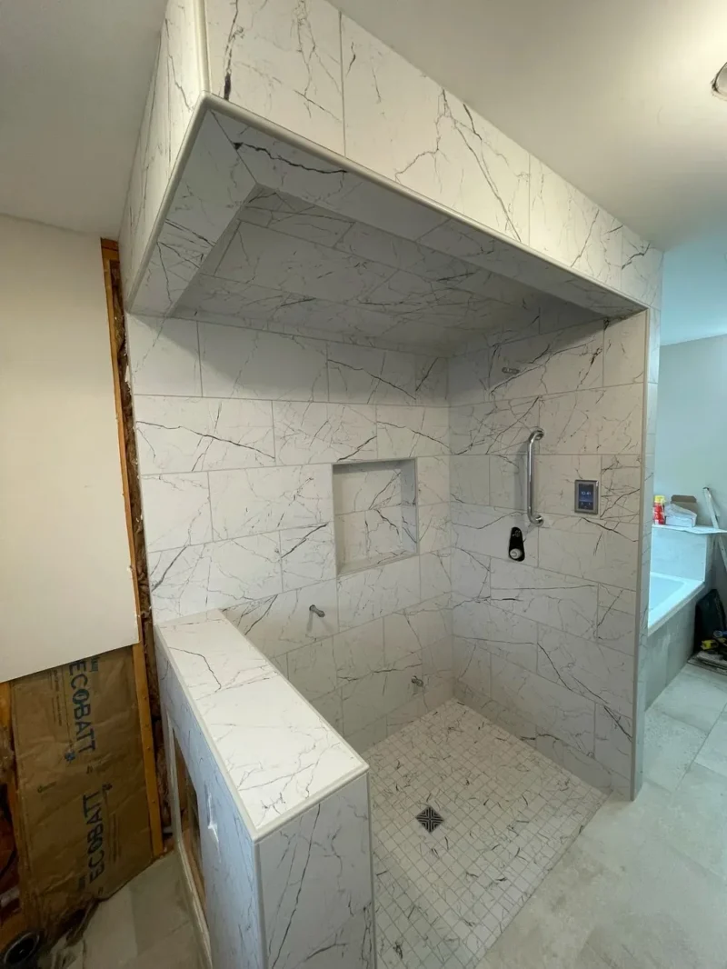 Luxurious spa-style walk-in shower with large-format marble-look tile, integrated bench, recessed niche, floating soffit, and sleek modern fixtures in a bright contemporary bathroom