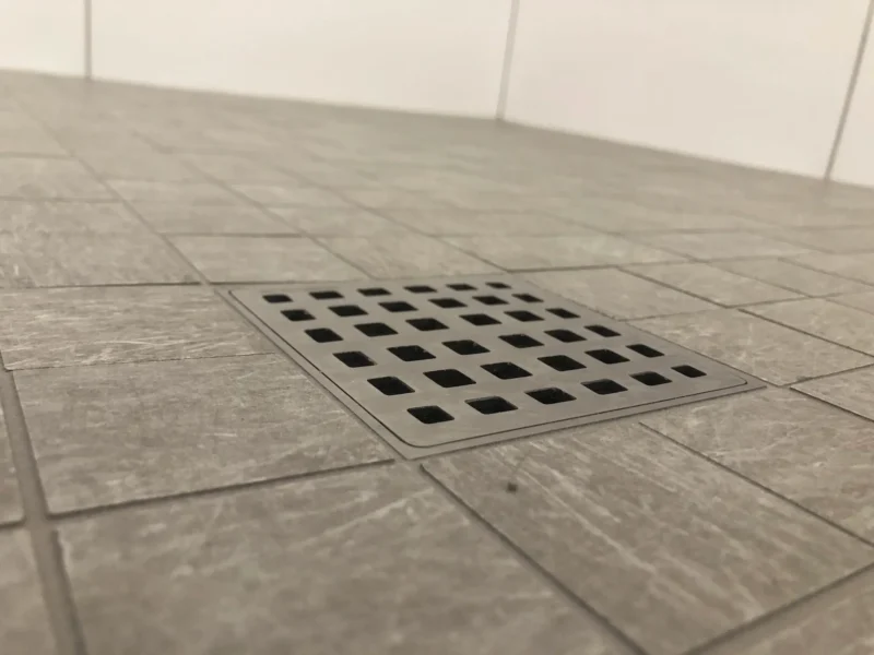 Close-up shower drain installation with gray tile flooring and precision grout alignment