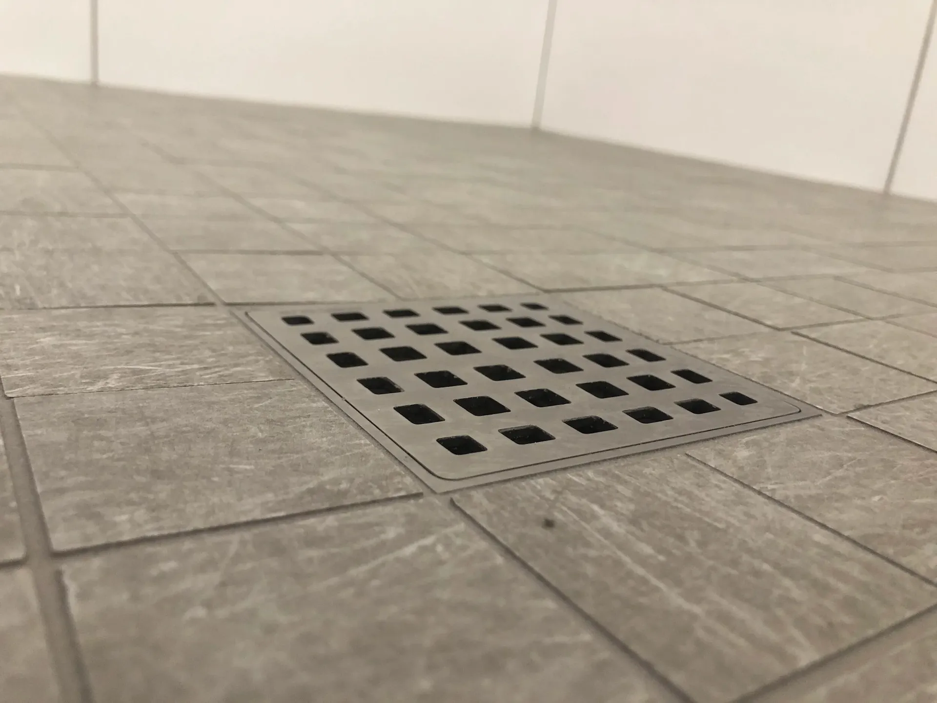 Close-up shower drain installation with gray tile flooring and precision grout alignment