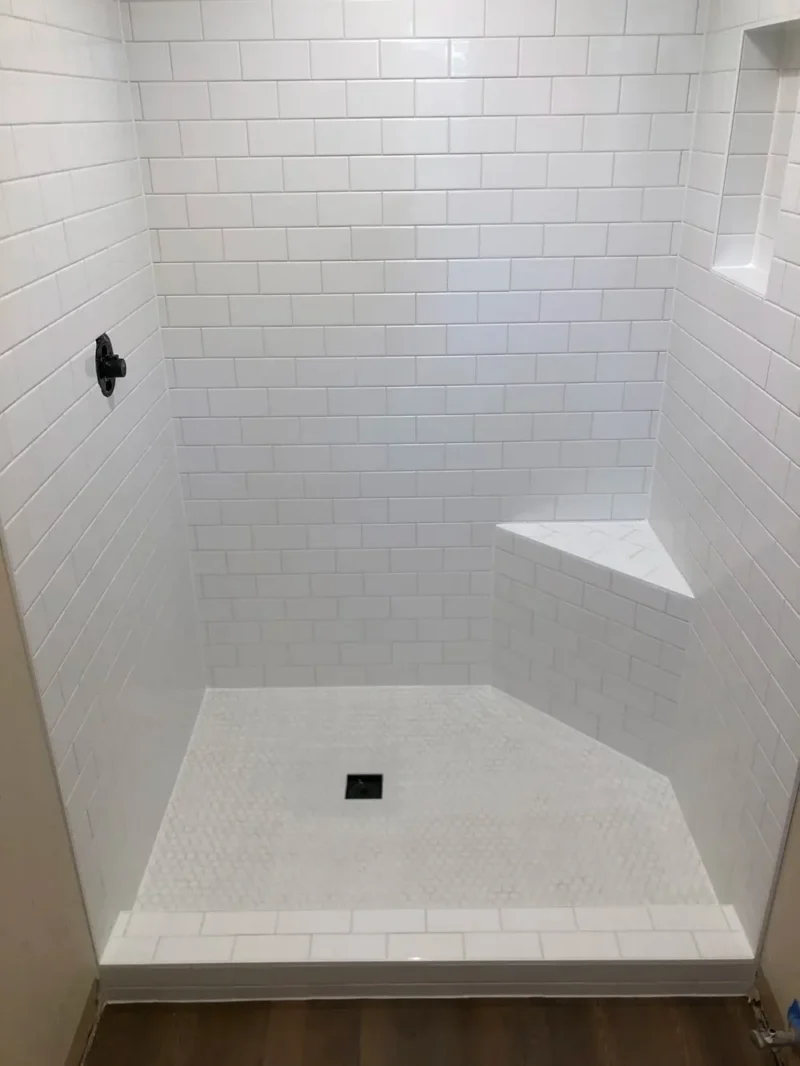Minimalist white subway tile shower featuring built-in bench, niche, and mosaic flooring