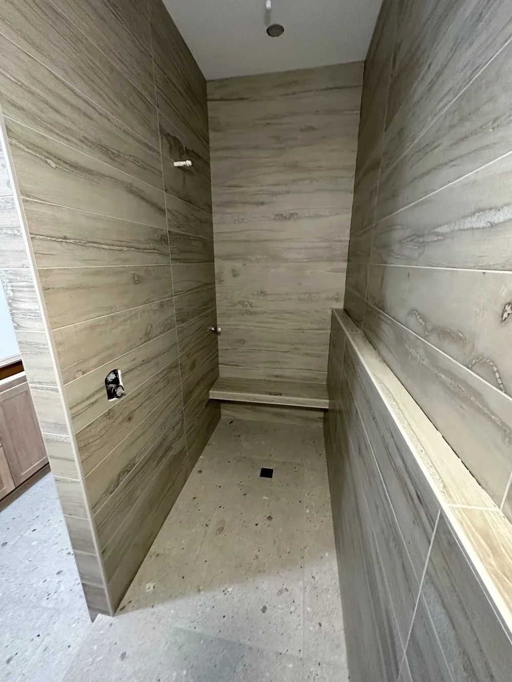 Contemporary walk-in shower featuring wood-look tile walls, terrazzo flooring, and floating bench