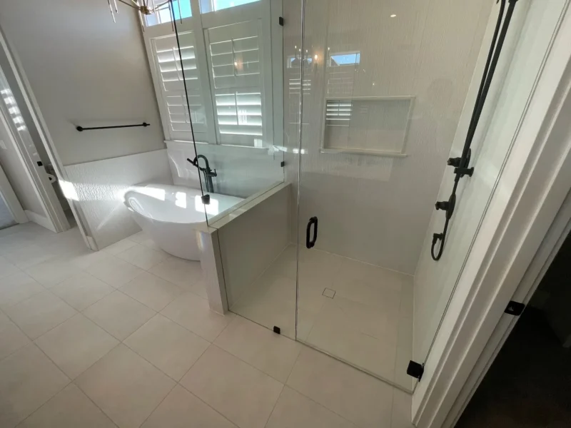 Bright modern bathroom with frameless glass shower, freestanding tub, and large plantation windows