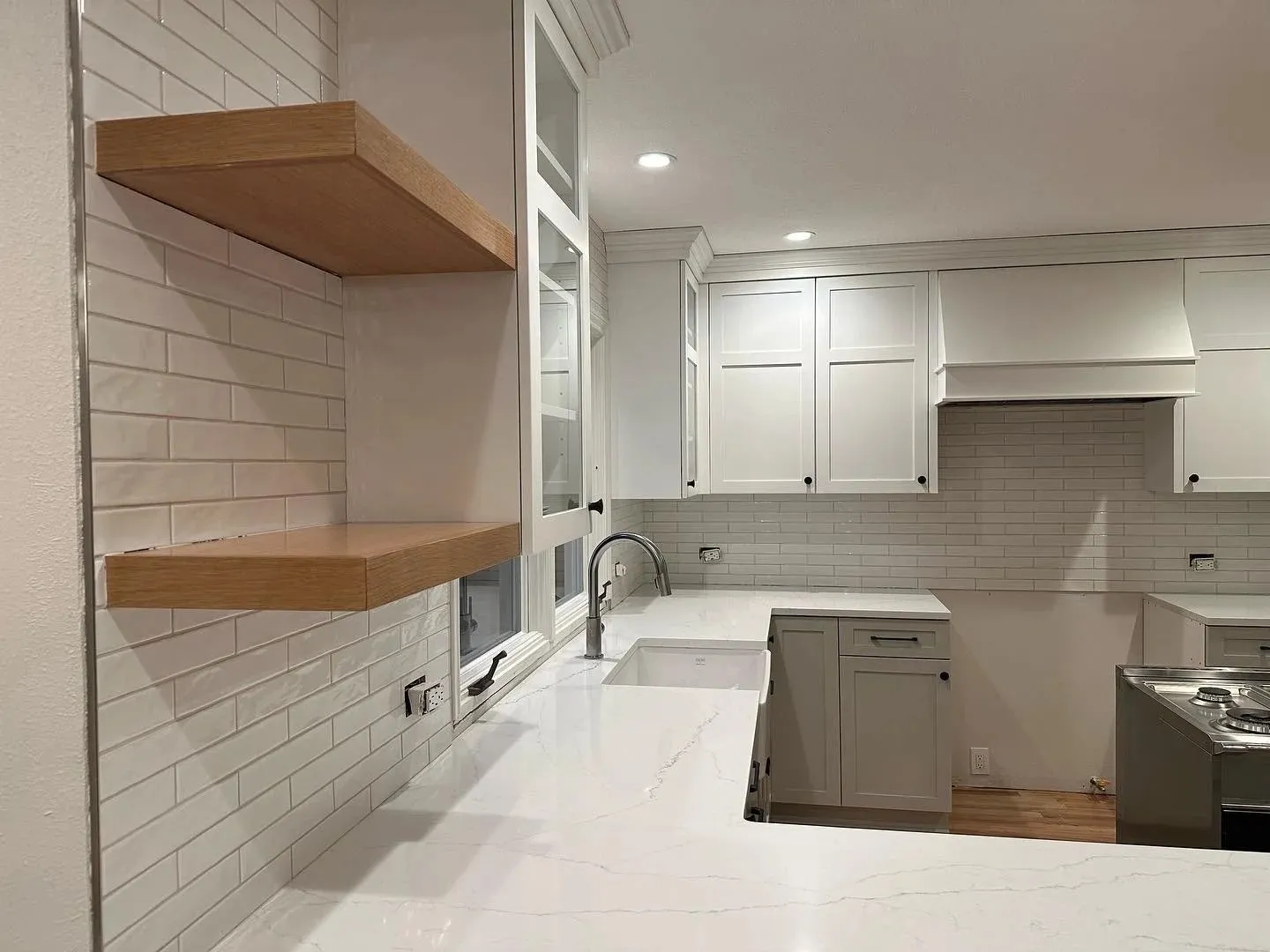Modern white kitchen with quartz countertops, subway backsplash, and floating wood display shelves