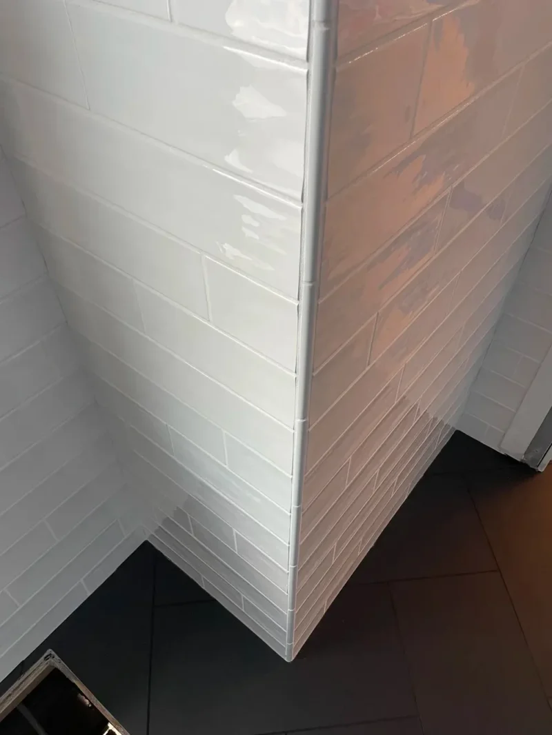 White glossy subway shower tile with rounded corners above dark modern floor tiles