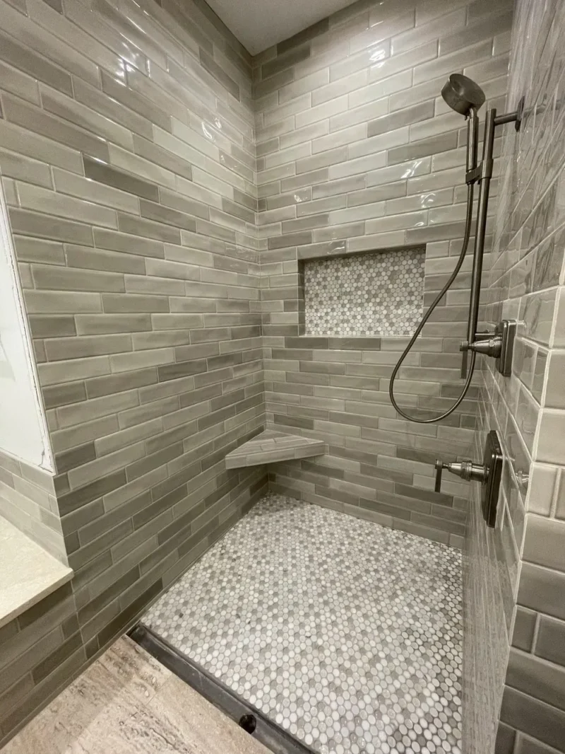 Gray subway tile shower with pebble floor and corner bench