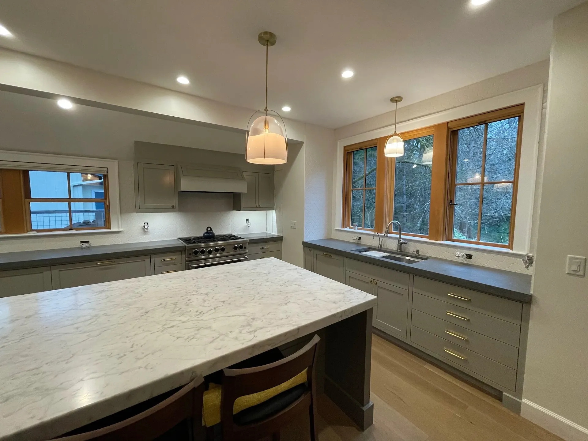 Modern farmhouse kitchen with quartz island, gray cabinetry, pendant lighting, and wood trim windows
