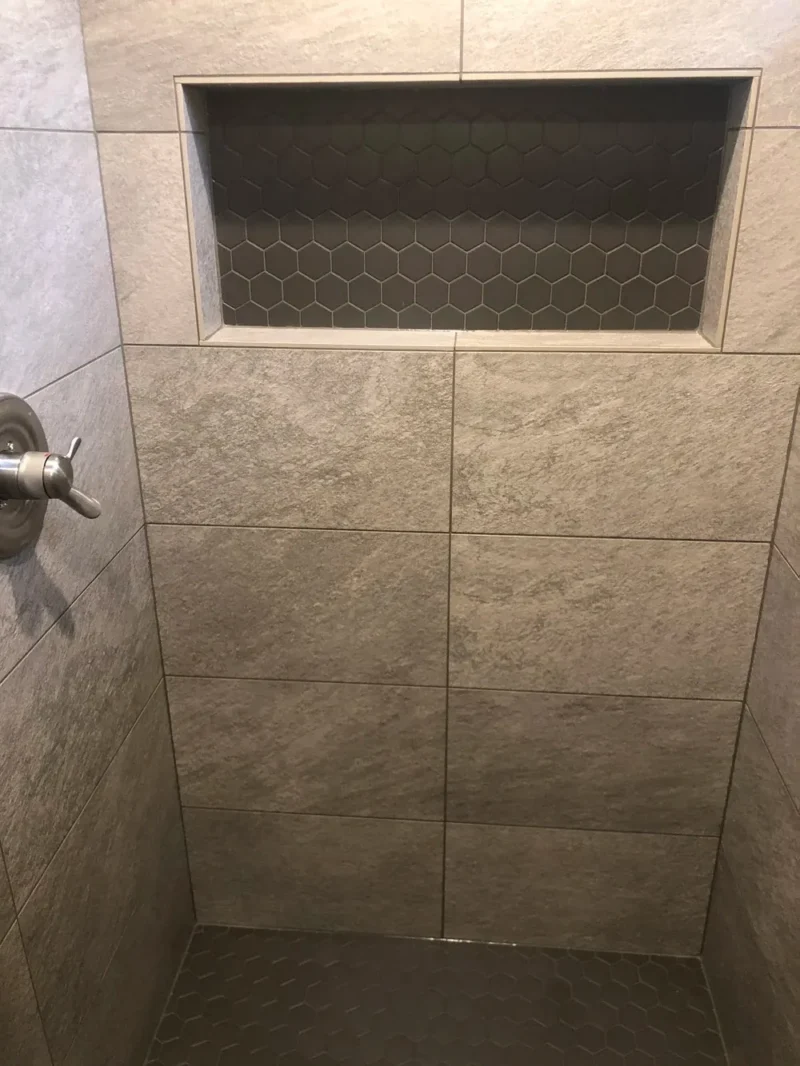 Contemporary tiled shower with recessed niche, gray porcelain walls, and black hexagon accents
