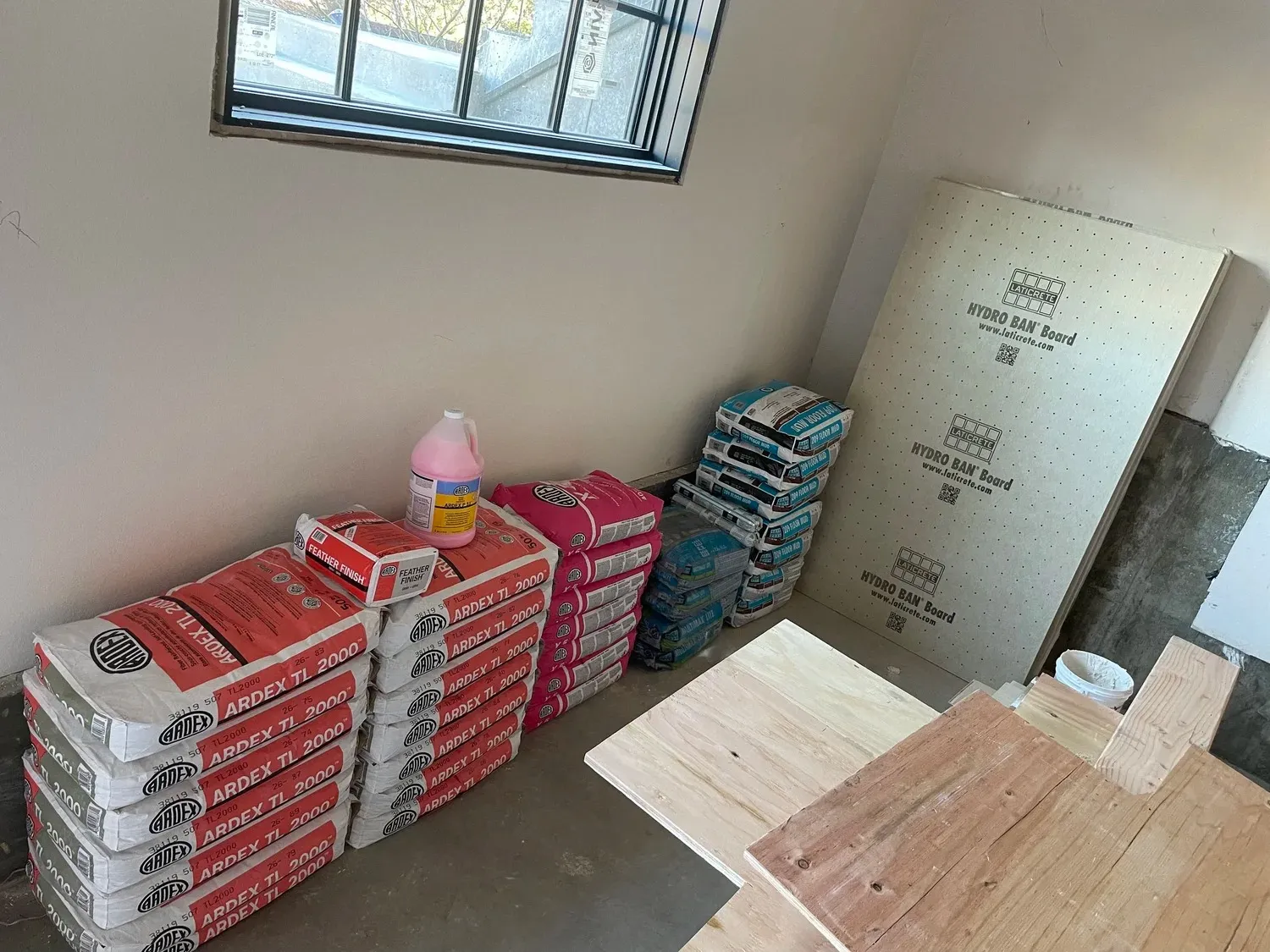 Tile installation materials including Ardex mortar, Hydro Ban boards, and large format porcelain tiles stacked indoors