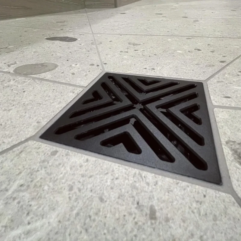 Black geometric shower drain on speckled gray tile floor